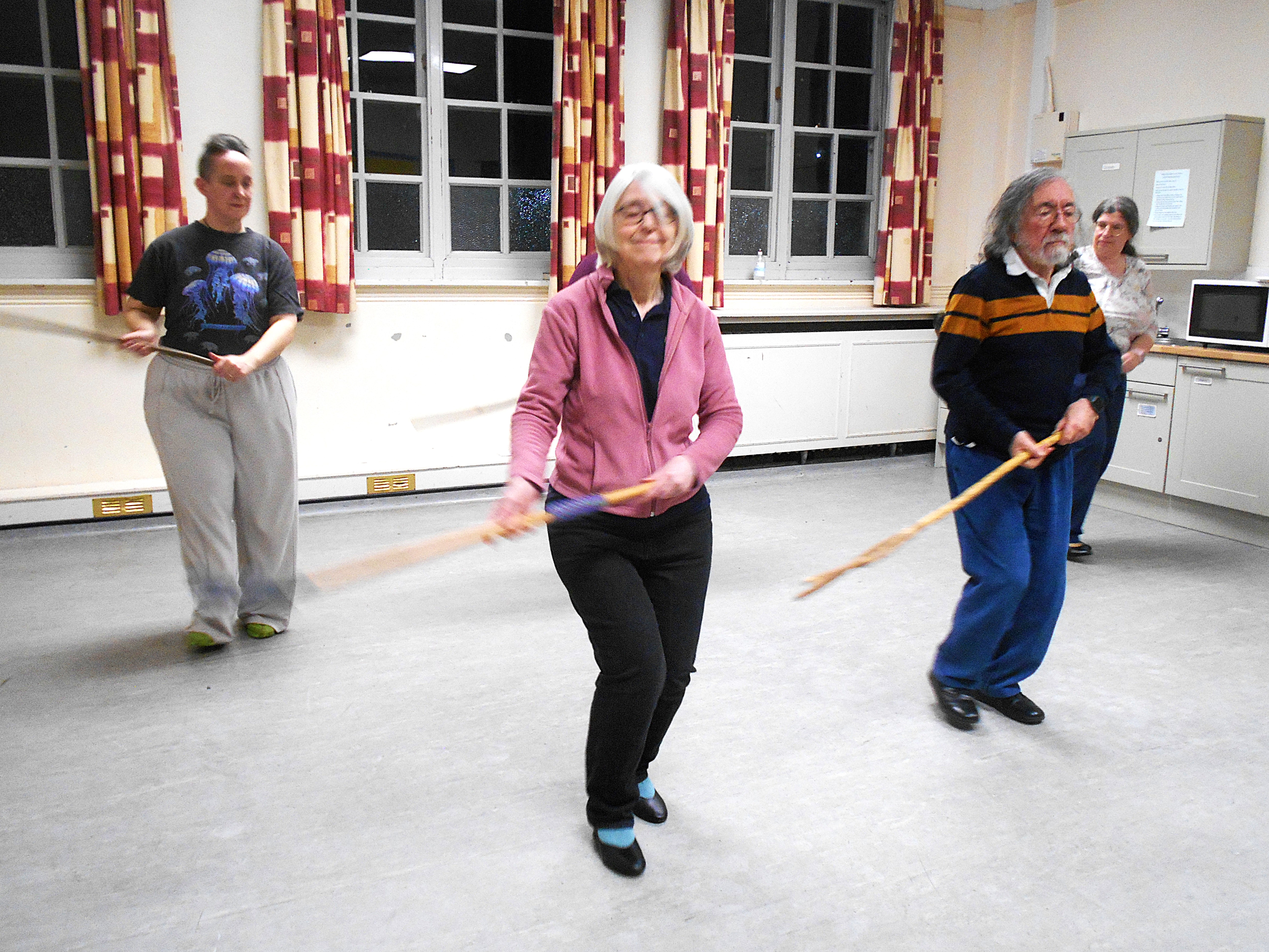 Dancers practising. Three dancers are shown practising a dance in a brightly lit room. They are holding long sticks.